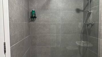 Une douche à l’italienne avec une porte en verre, un pommeau de douche à main et un autre pommeau de douche à main fixé au mur.
