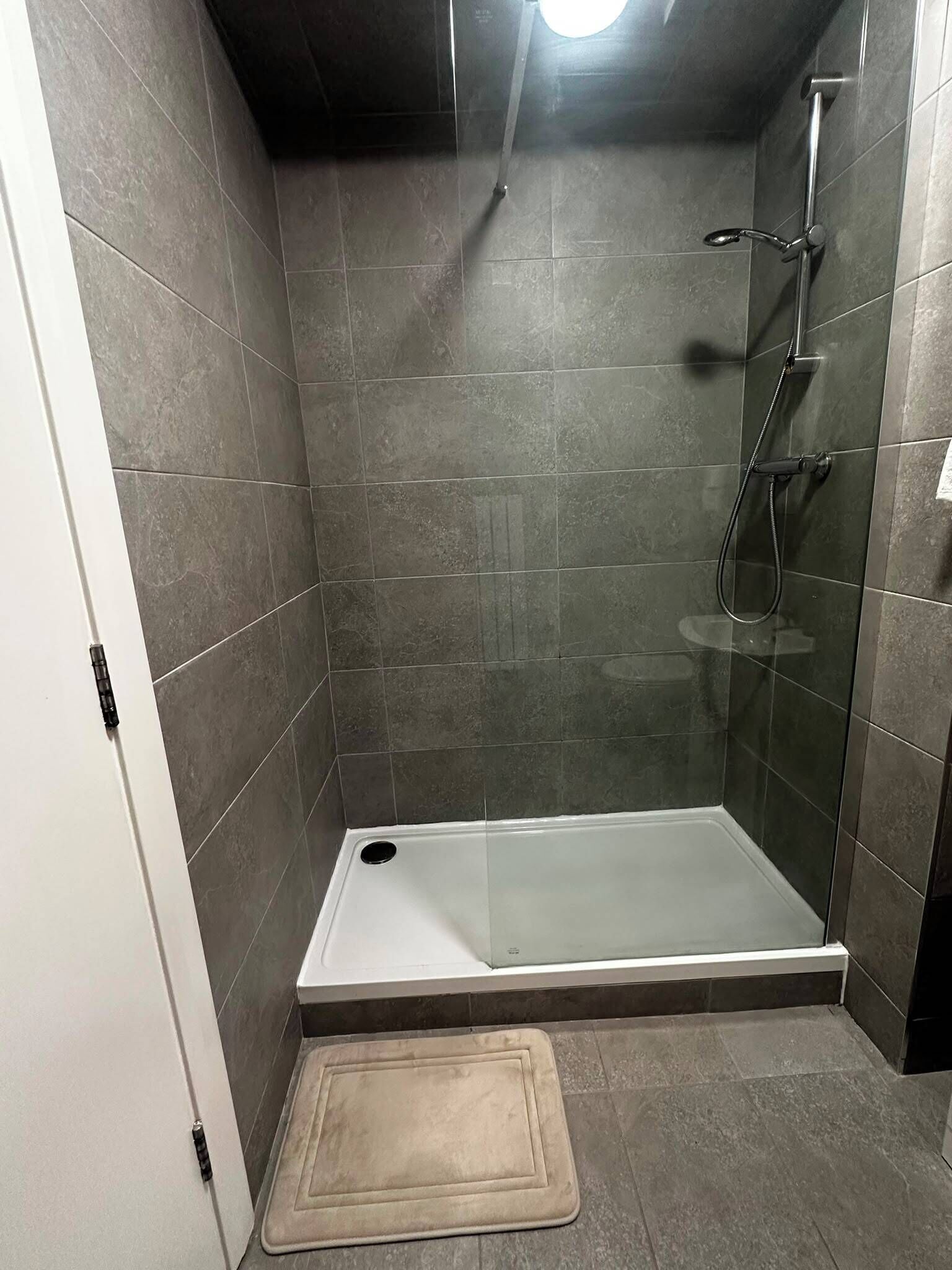 A shower with a glass door, a showerhead, and a handheld shower attachment.