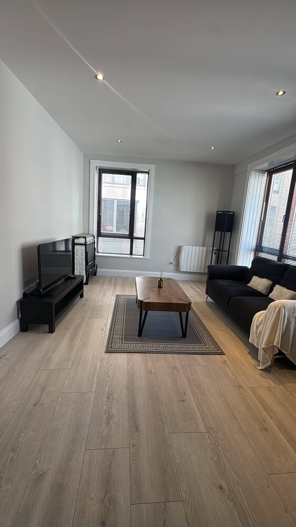 A modern living room with a flat-screen TV, a coffee table, a sofa, and a large window with blinds.