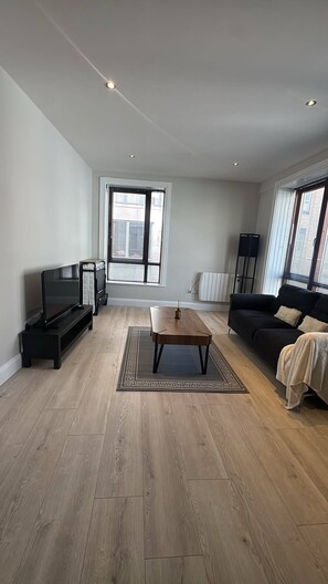 Una sala de estar moderna con un televisor de pantalla plana, una mesa de centro, un sofá y un amplio ventanal con persianas.