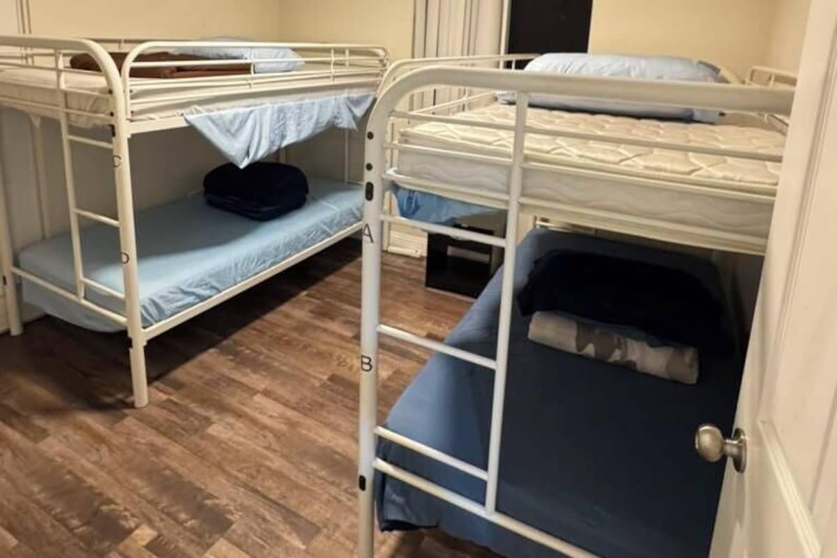 A room with bunk beds, wooden flooring, a white door, and a ceiling light.