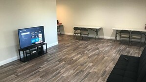 Une pièce comprenant un téléviseur à écran plat posé sur un meuble, un canapé noir et une table à manger avec des chaises.