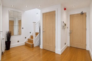 A hallway with wooden flooring, a staircase, and two wooden doors. - Luxury 3-Bed Penthouse · Sleeps 7 · Gated · NEC (Shirley)