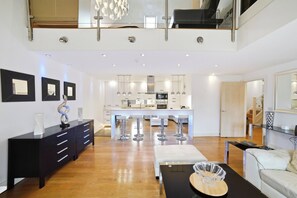 A modern interior with a dining area, kitchen, and a staircase leading to an upper level. - Luxury 3-Bed Penthouse · Sleeps 7  · Gated · NEC (Shirley)