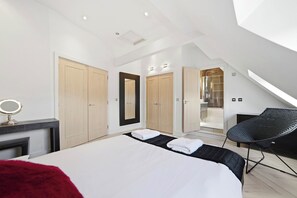 A modern bedroom with a large bed, a mirror, a chair, and a walk-in shower. - Luxury 3-Bed Penthouse · Sleeps 7 · Gated · NEC (Shirley)