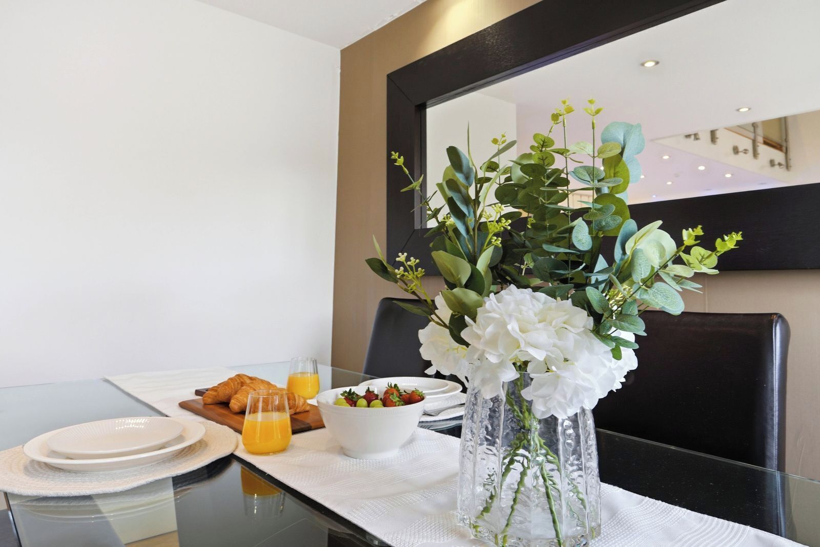 Un desayuno con croissants, un tazón de fruta y un vaso de jugo de naranja sobre una mesa con mantel blanco.