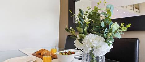 Un desayuno con croissants, un tazón de fruta y un vaso de jugo de naranja sobre una mesa con mantel blanco.