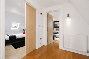 A hotel room with a bed, a small window, a radiator, and a door leading to another room. - Luxury 3-Bed Penthouse · Sleeps 7 · Gated · NEC (Shirley)