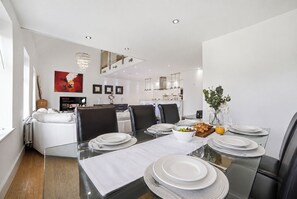 A modern dining area with a glass table, white plates, and a vase of flowers. - Luxury 3-Bed Penthouse · Sleeps 7 · Gated · NEC (Shirley)