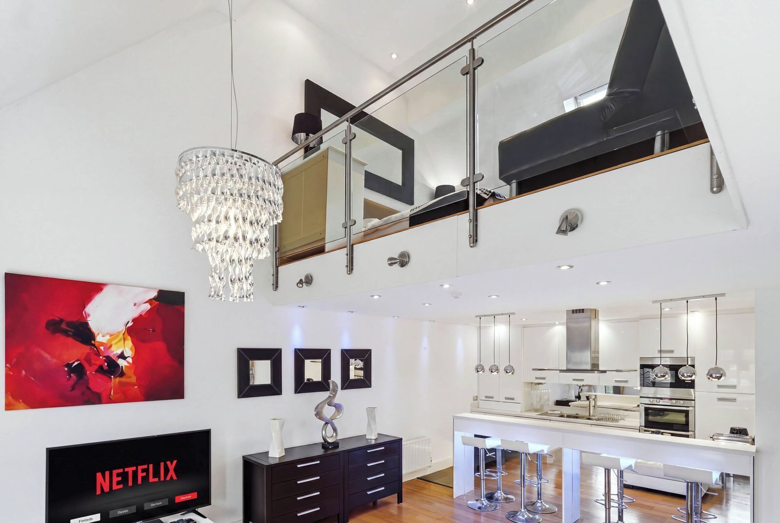 A modern kitchen with a central island, stainless steel appliances, and a glass railing above.