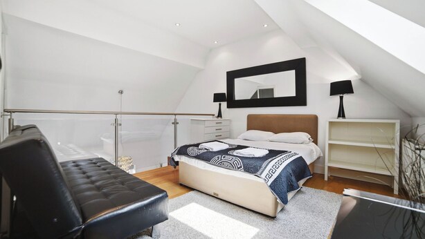 Een slaapkamer met een bed, een stoel, een bureau, een spiegel en een plank.