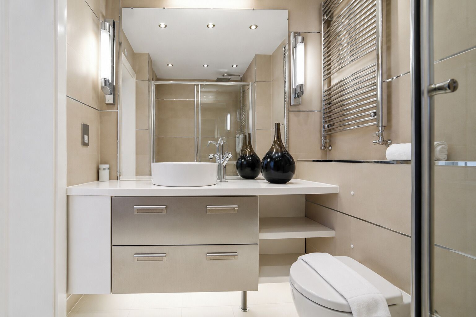 A modern bathroom with a white sink, two black vases, a toilet, and a glass shower enclosure.