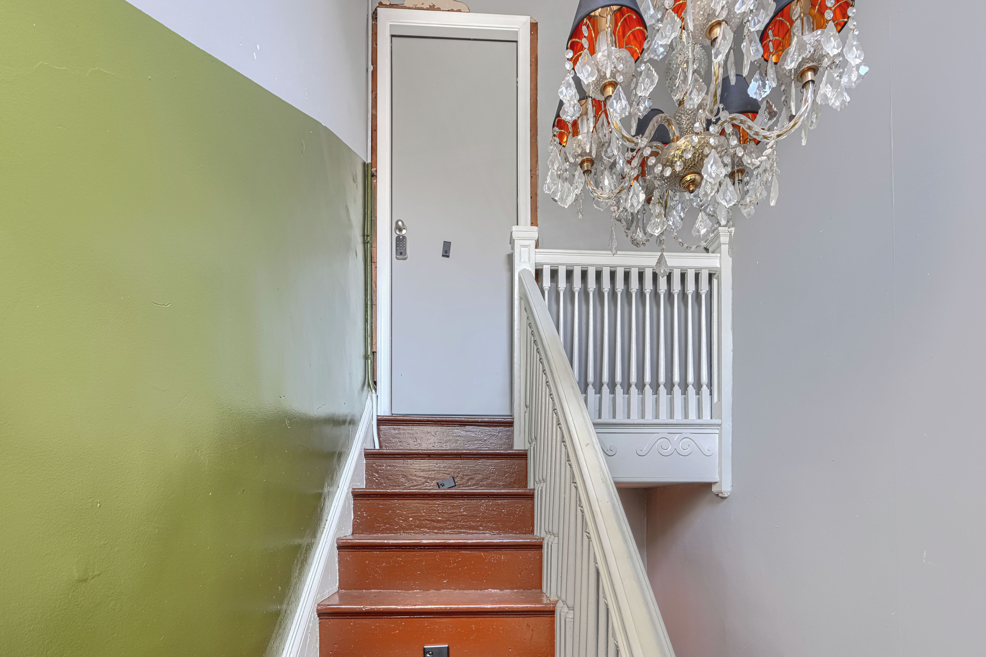A staircase with a white railing, a door with a keypad lock, and a chandelier with crystal decorations.