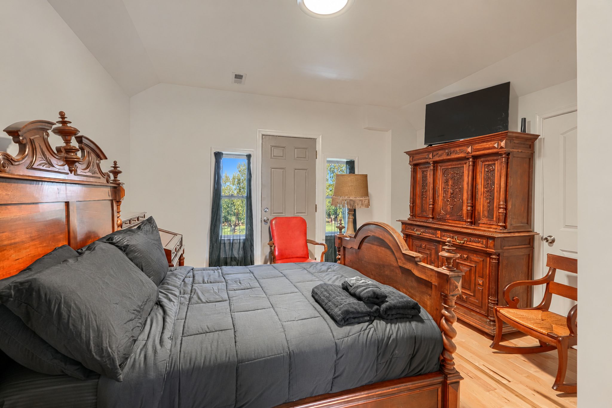 Une chambre à coucher avec un lit, une commode en bois, une chaise rouge et un téléviseur fixé au mur.