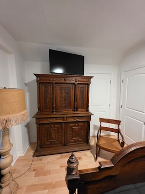 Une pièce comprenant un meuble en bois, un téléviseur fixé au mur, une chaise et un lit.
