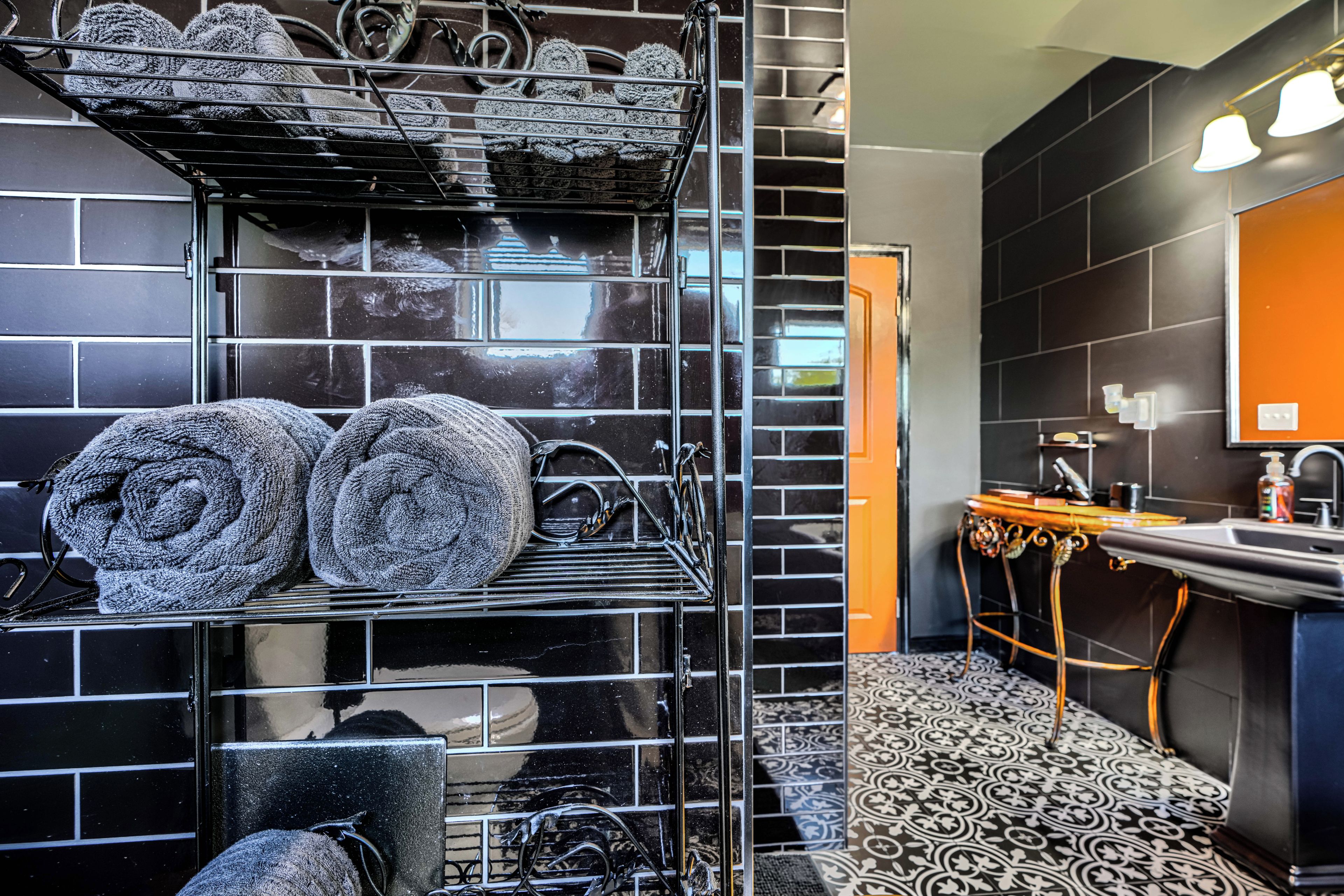 Une salle de bain avec un mur recouvert de carreaux noirs, un lavabo avec un miroir et un sol à motifs.