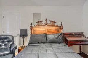 A bedroom with a wooden bed, a leather chair, a desk, and a lamp.