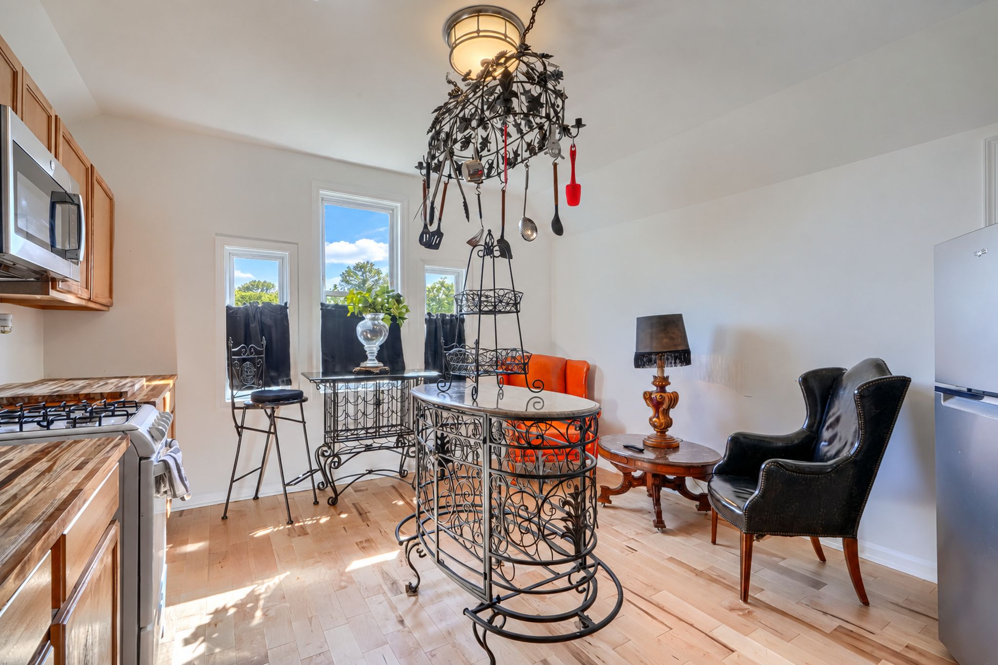 A kitchen with a stove, a dining table with chairs, a chandelier, and a refrigerator.