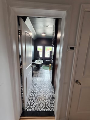 Un couloir menant à une salle de bain carrelée avec des motifs, équipée de toilettes et d’un lavabo.