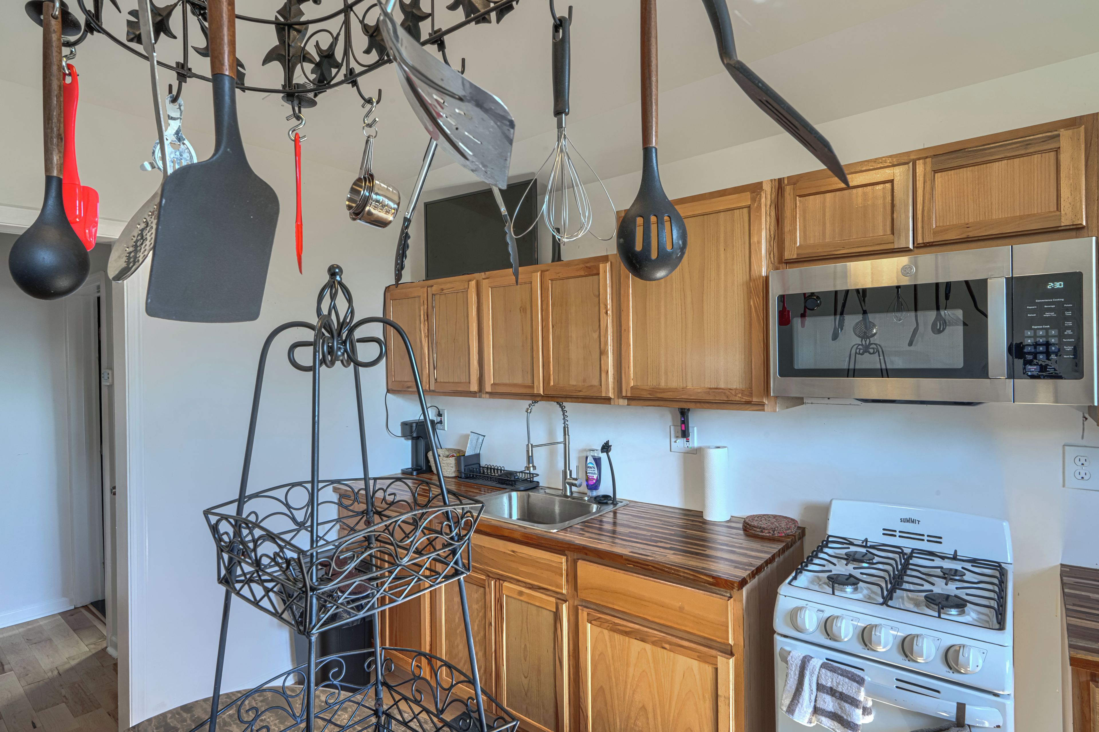 A kitchen with wooden cabinets, a stainless steel sink, a gas stove, and various hanging utensils.