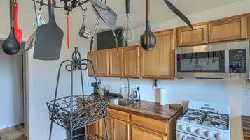 A kitchen with wooden cabinets, a stainless steel sink, a gas stove, and various hanging utensils.