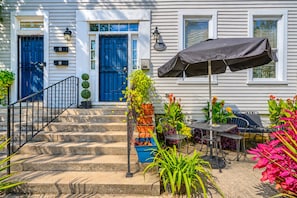 Uma casa com varanda frontal, escadaria e um pátio com móveis e plantas.
