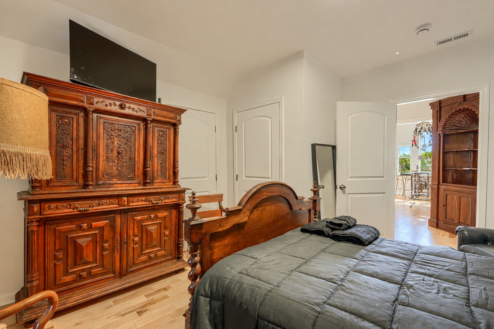 A bedroom with a large wooden dresser, a bed with a grey quilt, and a wooden wardrobe.