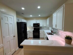 A modern kitchen with white cabinetry, a black refrigerator, a microwave, and a sink. - Newly Renovated 3BR+Sunroom, Sleeps 8. Walk to Downtown McKinney & Finch Park (McKinney)