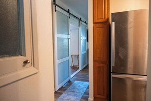 A kitchen with a stainless steel refrigerator, wooden cabinets, and a sliding glass door leading to a room. - Beautiful Beach Bungalow (Kihei)