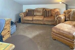 A living room with a brown leather sofa, a wooden side table, and a desk with a chair. - Scenic Mountain Village Stay - Hot Tub , Gym (Mountain Village)