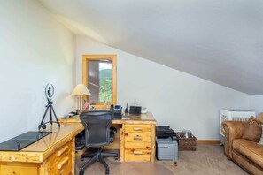 Ein Homeoffice mit Schreibtisch, Computer und Stuhl. Ein Fenster bietet Blick auf Grünflächen.
