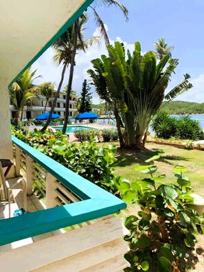 Ein Balkon mit Blick auf einen Pool, Palmen und ein Gebäude mit blauen Sonnenschirmen.