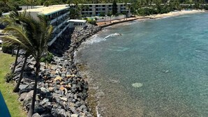 A coastal resort with a rocky shoreline, clear blue waters, and a backdrop of a green hill with buildings. - Ocean Front 2-bedroom condo in beautiful St Thomas (St Thomas)