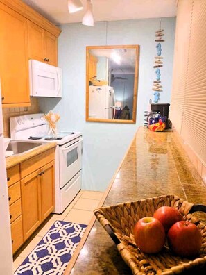 Una cucina con mobili in legno, un fornello bianco, un lavello e un piano di lavoro con un cesto di mele.
