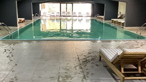 Una piscina interior con agua cristalina, rodeada de sillas de descanso y suelo de baldosas.