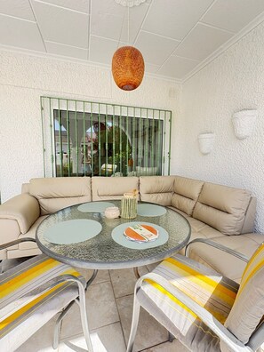 A round glass table with a beige sofa and striped cushions, a woven pendant light, and a window with green metal bars. - Townhouse in a quiet neighborhood (El Chaparral)