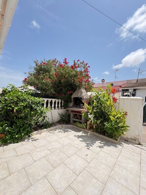 A patio area with a tiled floor, a stone wall, and a variety of plants including a flowering bush. - Townhouse in a quiet neighborhood (El Chaparral)