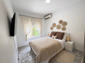 A bedroom with a bed, a bedside table, a wall-mounted TV, a window with curtains, and a wall decoration. - Townhouse in a quiet neighborhood (El Chaparral)