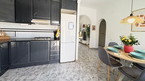 A modern kitchen with dark cabinets, a white refrigerator, and a dining area with a wooden table and chairs. - Townhouse in a quiet neighborhood (El Chaparral)