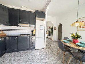 A modern kitchen with dark cabinets, a white refrigerator, and a dining area with a wooden table and chairs. - Townhouse in a quiet neighborhood (El Chaparral)