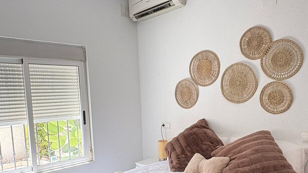 A bedroom with a large bed, a window with blinds, an air conditioning unit, and decorative wall hangings. - Townhouse in a quiet neighborhood (El Chaparral)