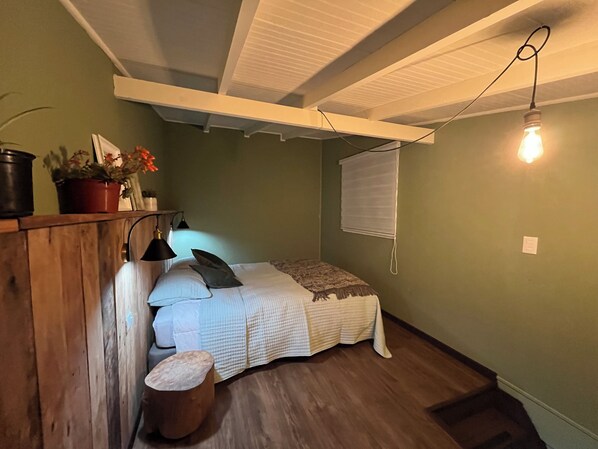 A bedroom with a bed, bedside table, lamp, and a small stool.