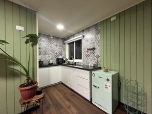 A compact kitchen with a window, a refrigerator, and a potted plant. - Casita Nalca / Canasto de Agua Huts—Chaitén, Chilean Patagonia. (Chaiten)