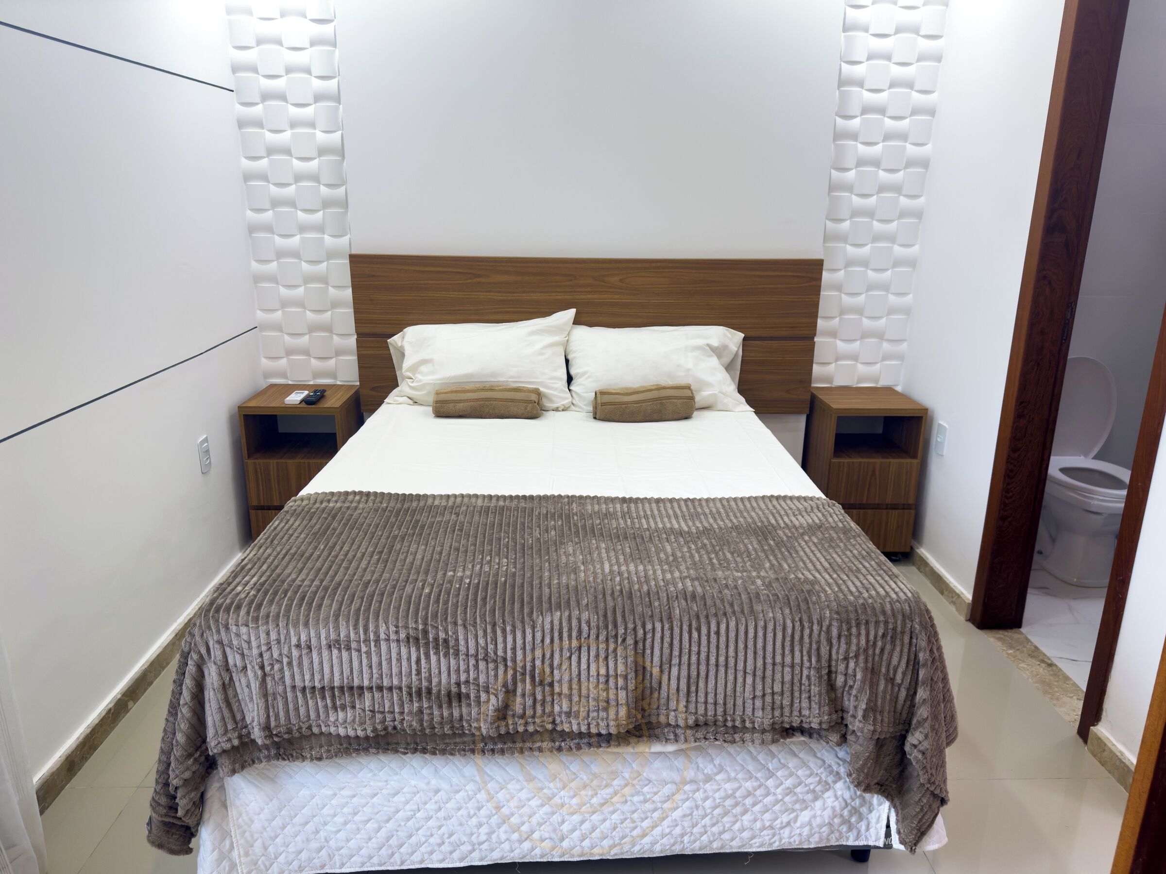 A neatly made bed with a brown blanket, two bedside tables with lamps, and a wooden headboard.