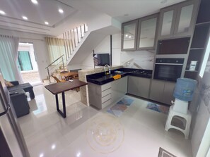 A modern kitchen with a dining area, a water dispenser, and a built-in oven. - Taperapuã Beach - Ashby Houses (Porto Seguro)