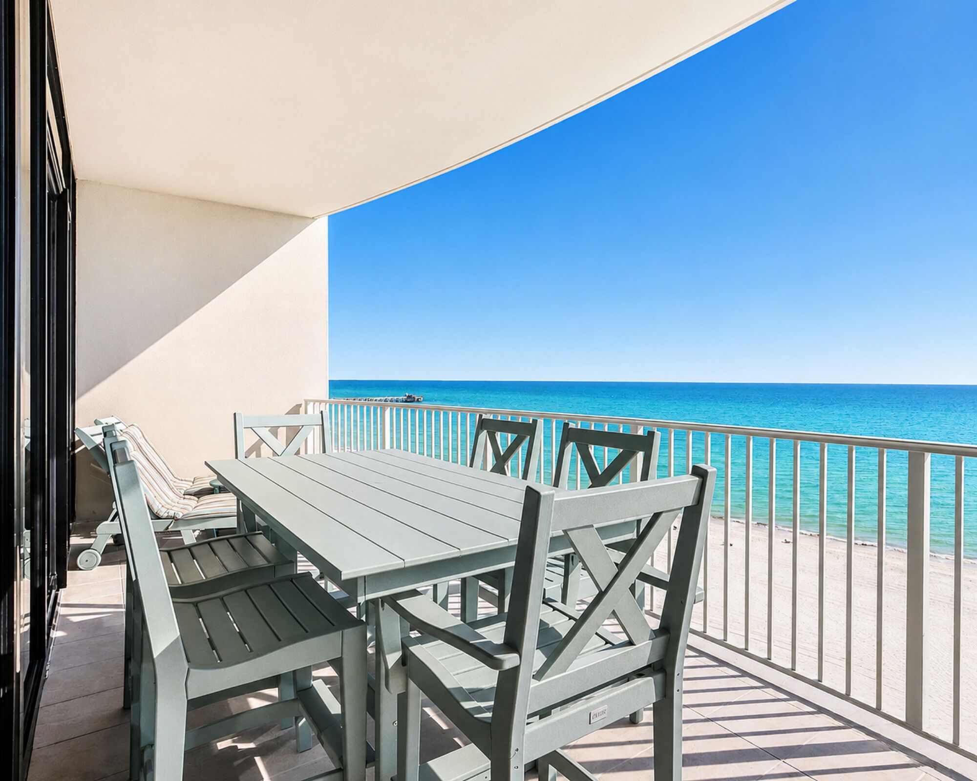 A balcony with a table and chairs, overlooking a clear blue sea.