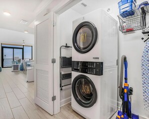 A modern laundry room with two stacked washing machines, a dryer, and a vacuum cleaner. - Phoenix GS II #1003 - Luxury Beachfront 3BR, Lazy River, Heated Pool, Hot Tub (Gulf Shores)