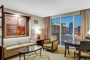 A hotel room with a city view, a sofa, a chair, a table, and a painting on the wall. - MGM Signature-27-705 F1 Track & Strip View Balcony (Las Vegas)