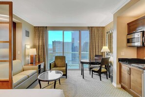 A hotel room with a balcony, a dining area, a sofa, a coffee table, and a kitchenette. - MGM Signature-27-705 F1 Track & Strip View Balcony (Las Vegas)