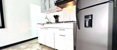 Una cocina con armarios blancos, un refrigerador de acero inoxidable, un microondas y una estufa a gas.